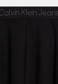 Svart bomulls t-shirt med en framträdande grå "Calvin Klein Jeans"-logotyp längs kragen, med en mjuk textur och figurnära design.