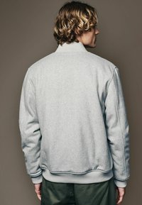 Light grey fleece jacket with ribbed collar and cuffs; features a casual silhouette and subtle texture on the fabric.