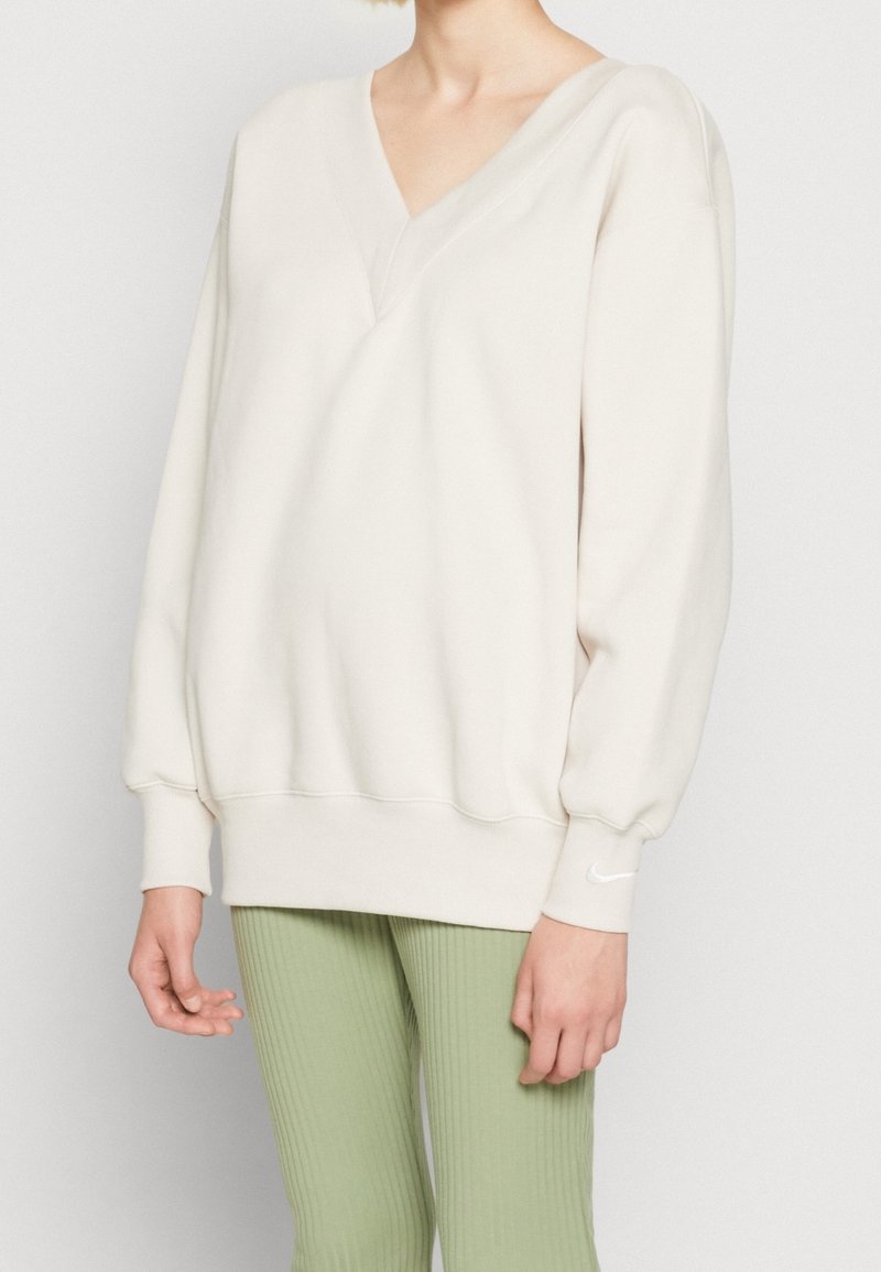 Light beige sweatshirt with a V-neck, oversized sleeves, and ribbed cuffs, paired with textured green leggings. Soft fabric, casual design.