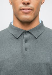 Gray polo shirt with a soft texture, featuring a collar, three buttons, and a light blue underlayer visible at the neckline.