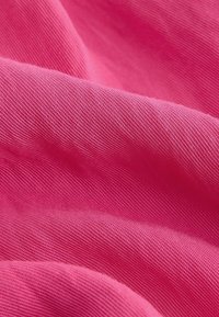 Gros plan d'un tissu rose vif avec un tissage texturé visible et des plis doux créant des variations de lumière et d'ombre.