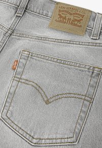 Γκρι τζιν από τζιν ύφασμα, με πίσω τσέπη που έχει χαρακτηριστικό σχέδιο με ραφές, καφέ δερμάτινο ταμπελάκι με το εμπορικό σήμα και πορτοκαλί ετικέτα.