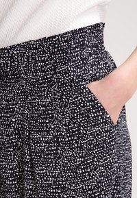 Czarne spodnie z białym, nakropionym wzorem, z elastycznym paskiem w talii i bocznymi kieszeniami. Wykonane z miękkiego, strukturalnego materiału.