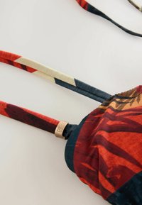 Viacfarebný bikiny top s kvetinovými vzormi, nastaviteľné ramienka v červenej a modrej farbe a bronzový dizajnový prvok pri ramienku.