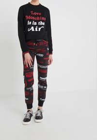 Czarna bluza z nadrukiem "Love Moschino is in the Air"; czerwono-czarne dresy z różnorodnymi wzorami logo; czarne sneakersy.