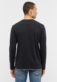 Zwarte lange mouwen shirt met ronde hals, gemaakt van katoen, met een gladde textuur. Gekleed met blauwe jeans, gezien vanuit de achterkant.