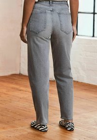 Graue hochgeschnittene Jeans mit geradem Schnitt und zwei Gesäßtaschen. Kombiniert mit schwarz-weiß gestreiften Zebra-Druckschuhen.