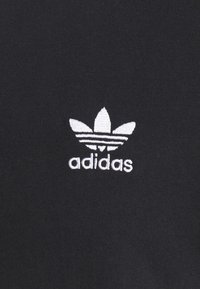 Černá látka s bílým vyšitým logem Adidas Trefoil a textem "adidas" ve středu.