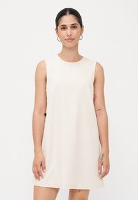 Rochie tunică fără mâneci, de culoare crem, dintr-un material neted, cu un guler rotund și o silueta dreaptă. Detalii subtile pe tiv.