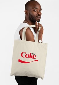 Beige katoenen tas met dikke handvatten, met een prominent rood "Diet Coke" logo en een gebogen rode accent aan de voorkant.