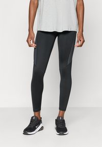 Schwarze Sportleggings mit Netzpaneelen an den Seiten, einer glatten Textur und einem figurbetonten Design. Getragen mit einem hellgrauen T-Shirt und schwarzen Sneakers.