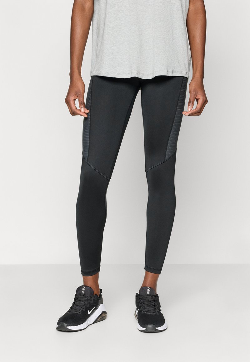 Schwarze Sportleggings mit Netzpaneelen an den Seiten, einer glatten Textur und einem figurbetonten Design. Getragen mit einem hellgrauen T-Shirt und schwarzen Sneakers.