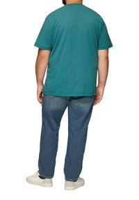 Turkusowa bawełniana koszulka z krótkim rękawem, luźny krój i okrągły dekolt, w zestawie z niebieskimi dżinsami i białymi sneakersami.