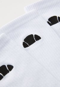 Calze bianche alla caviglia con dettagli del logo ricamato in nero. Presentano un bordo a costine e un tessuto morbido e texturizzato.