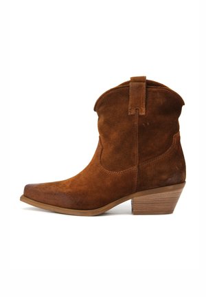 Stivale alla caviglia in suede marrone con punta affusolata e tacco in legno impilato. Presenta una linea superiore curva e un'apposita linguetta sul retro.