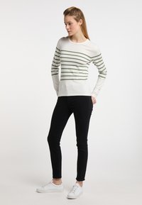 Sweter w paski w kolorze kremowym i zielonym z długimi rękawami, połączony z czarnymi spodniami typu slim fit i białymi sneakersami. Gładka faktura, okrągły dekolt.