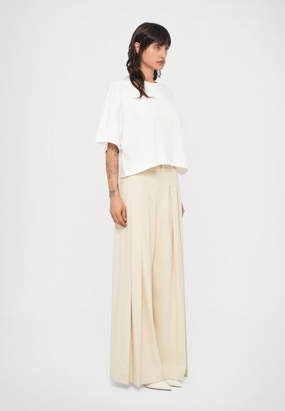 Λευκό κοντομάνικο κροπ τοπ συνδυασμένο με μπεζ, πλισέ παντελόνι φαρδιάς γραμμής, δημιουργώντας μια άνετη σιλουέτα.