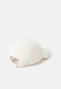 Cappellino da baseball in corduroy bianco con visiera curva, cinturino regolabile sul retro e piccoli fori di ventilazione nella parte superiore.