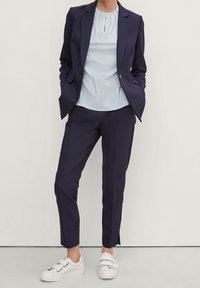Blazer navy y pantalones ajustados con una blusa de rayas de color azul claro, combinados con zapatillas blancas con doble correa. Tejido suave, diseño ceñido.