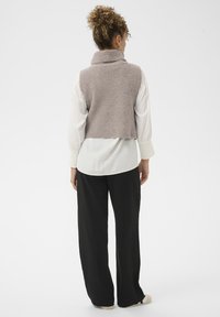 Rövidített, világos lila kötött mellény magas gallérral, fehér ing fölött viselve, fekete bőszárú nadrággal párosítva. Simább textúra.