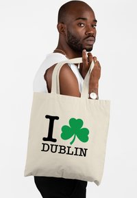Canvas draagtasje in natuurlijke kleur met zwarte tekst "I DUBLIN" en een groen klavertje ontwerp. Heeft stevige handvatten en een eenvoudige, functionele vorm.