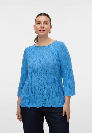Pull en tricot bleu avec une coupe amélée, présentant un motif en losanges, des manches 3/4 et un ourlet festonné. Porté sur un jean foncé.