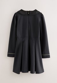 Vestito nero a maniche lunghe con gonna plissettata, colletto smerlato, cerniera posteriore e dettaglio di piping bianco sui polsini.
