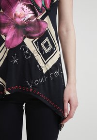 Black shirt featuring a large pink orchid graphic, with geometric beige accents and the text "Believe in yourself" embellished with sequins.