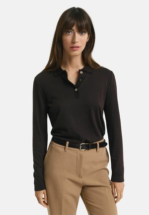 Polo shirt nero a maniche lunghe con colletto e patta a tre bottoni. Abbinato a pantaloni beige su misura e una cintura nera.