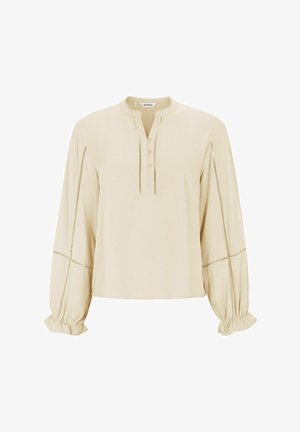 Blouse beige à manches longues avec un col rond, patte de boutonnage et poignets froncés. Présente des surpiqures décoratives le long des coutures.