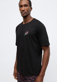 Tricou negru din bumbac cu decolteu rotund și mâneci scurte, având un design grafic colorat cu cireșe pe piept.