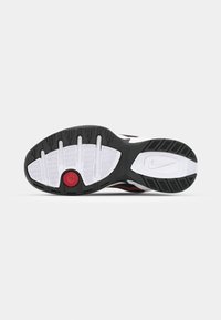 Talpa de încălțăminte sport Nike, cu o bază din cauciuc negru, un model texturat alb proeminent și un buton accent roșu în centru.