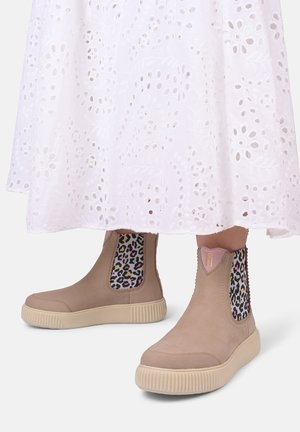 Beige ankelstøvler med leopardmønstret elastikpaneler, tekstureret læder og en kraftig cremefarvet sål, parret med en hvid øjeblikk lace-kjole.