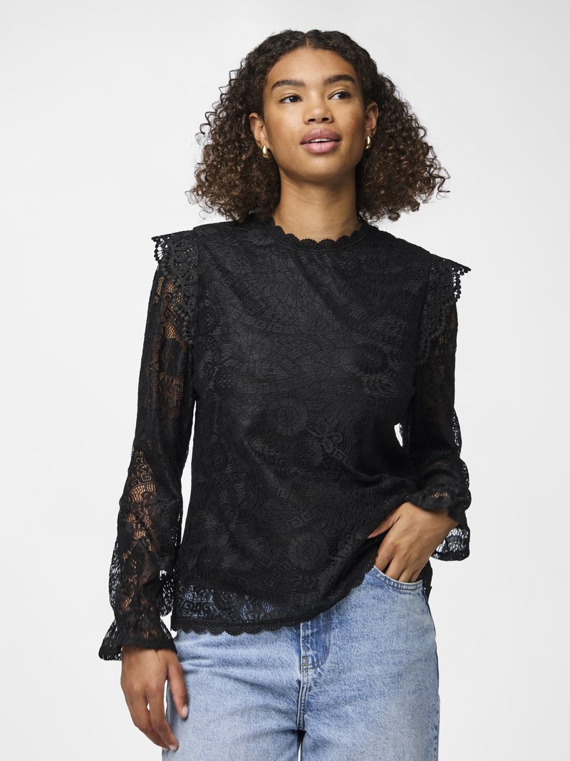 Svart bluse i blonde med en bølget halskant, lange ermer med volanger ved ermene, og blomster mønster. Kombinert med lyseblå denimjeans.