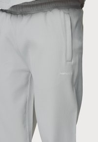 Grå ribbade träningsbyxor med elastisk midja, sidofickor och diskret broderad logotyp på det nedre benet. Strukturerad tygdetalj.