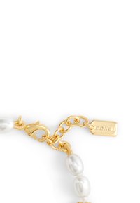 Bracelet enchaîné doré avec des perles blanches lisses et un fermoir à lobster, accompagné d'une étiquette rectangulaire gravée du mot "COACH".