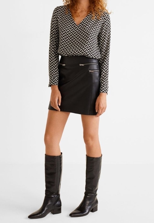 Top de manga larga con estampado en blanco y negro con escote en V, combinado con una mini falda de cuero negro con detalles de cremallera. Botas negras hasta la rodilla.
