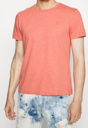 T-shirt corail à manches courtes en tissu texturé, avec un col rond et un logo discret sur la poitrine, associé à un jean déchiré bleu clair.