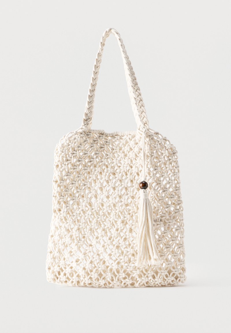 Sac fourre-tout en coton blanc tissé avec des poignées tressées et un pompon suspendu orné d'un détail en perle de bois.