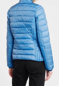 Jasnoniebieska kurtka puchowa z pikowanym wzorem, wysokim kołnierzem i dopasowanym krojem. Materiał ma gładką, błyszczącą strukturę z minimalnymi detalami.