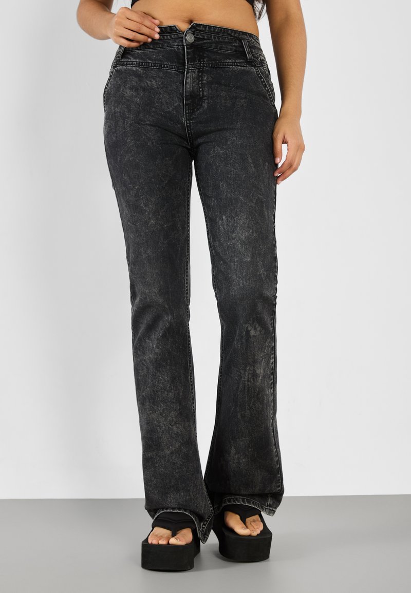 Jeans negros acampanados con textura desgastada y un sutil desvanecimiento, que cuentan con una cintura alta, detalles de costura y bolsillos frontales.