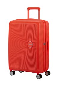 Valigia rigida di un rosso brillante con texture a cerchi concentrici, quattro ruote girevoli, un manico telescopico e una combinazione laterale per la chiusura.
