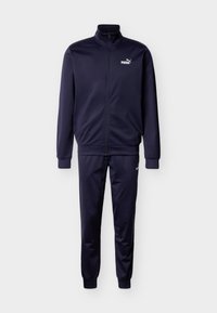 Σκούρο μπλε φόρμα από απαλό ύφασμα· διαθέτει ψηλό γιακά, πλήρη φερμουάρ και ριμπ μανσέτες· περιλαμβάνει λευκό λογότυπο στο στήθος και στο μηρό.