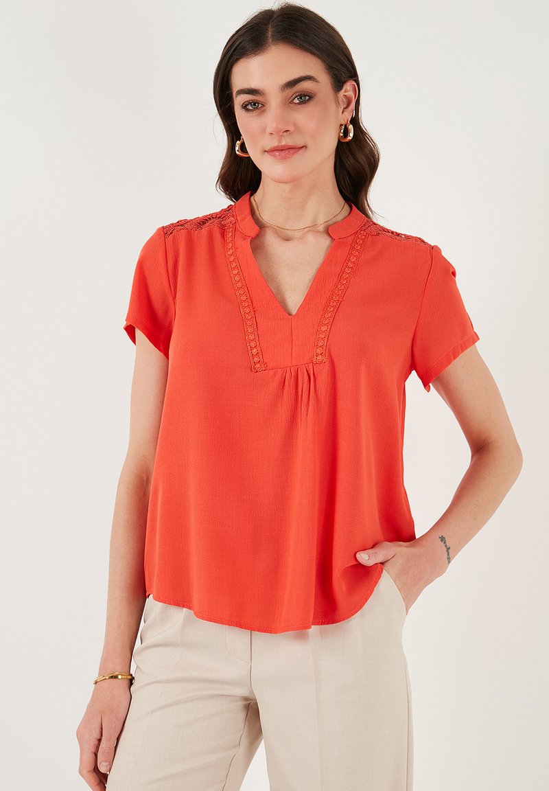 Top a maniche corte, scollo a V in un vivace tessuto arancione con bordo testurizzato lungo il collo, vestibilità comoda e una texture liscia e leggera.
