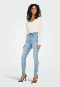 Lyseblå skinny jeans med høj talje, blødt denimstof og diskret falmning. Sammen med en langærmet hvid top og spidse hæle.
