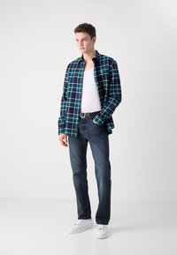 Camisa de franela a cuadros en tonos marino, verde y blanco, con una camiseta blanca por debajo; combinada con jeans oscuros y zapatillas blancas.