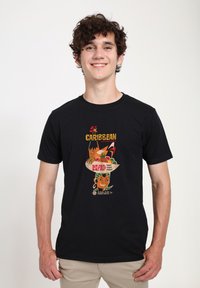 Černé bavlněné tričko s barevným grafickým designem s ilustracemi a textem inspirovanými Karibikem, vyobrazené na modelu proti neutrálnímu pozadí.