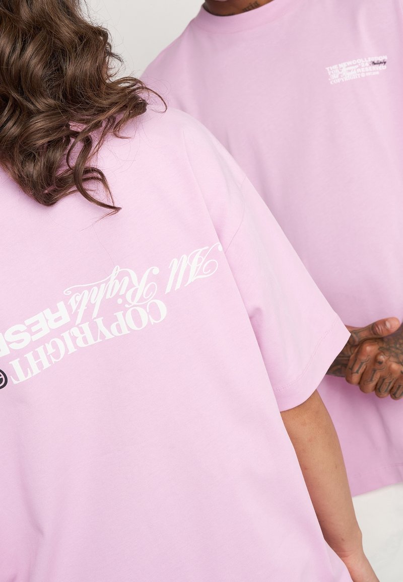 Deux personnes portant des t-shirts violet clair avec un texte de droits d'auteur blanc, l'une tournée de dos montrant l'impression au dos, l'autre partiellement visible de face.