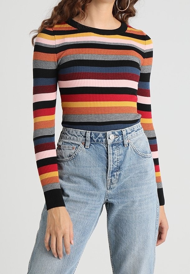 Femme portant un pull côtelé ajusté à manches longues avec des rayures horizontales colorées et un jean bleu clair taille haute.