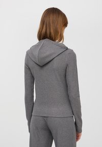 Szara bluza z kapturem wykonana z żebrowanej tkaniny, dopasowany krój, długie rękawy i teksturowany kaptur. Widok z tyłu, ukazujący detale przeszyć.